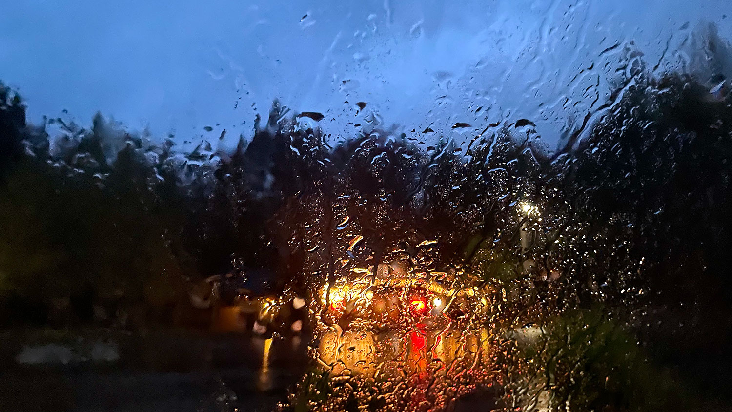 A rain-spattered windscreen in the evening, with a view of lights