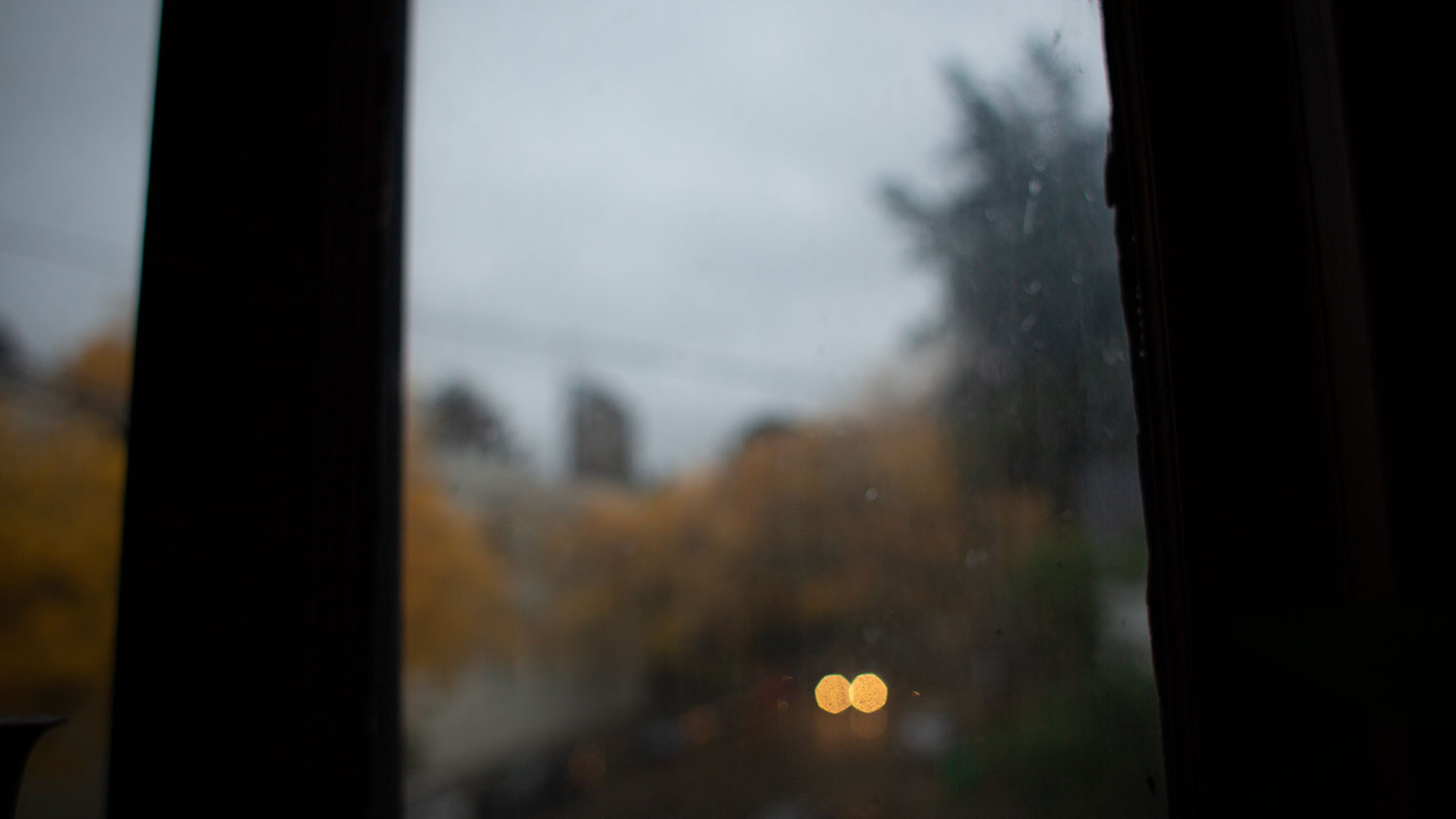 A rather dreary view from a small window, with car headlights coming down the road