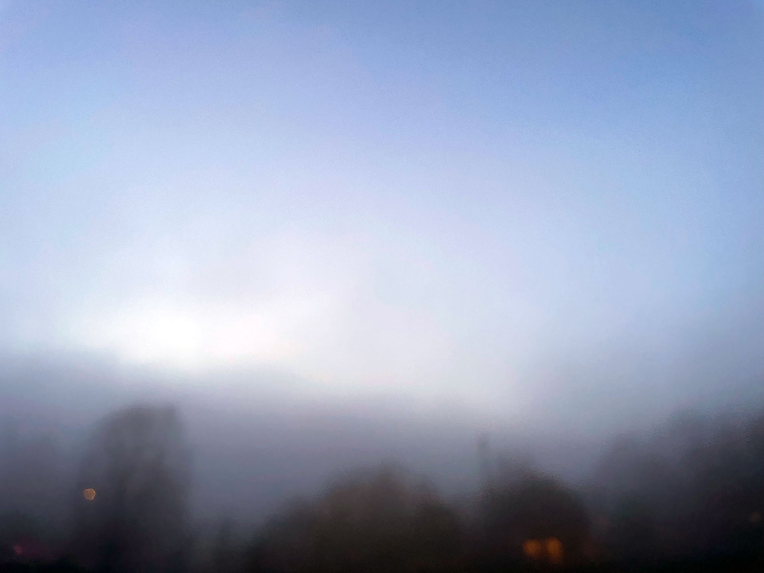 A periwinkle spring sky softened by a morning mist, dark shadows of trees and buildings a blur