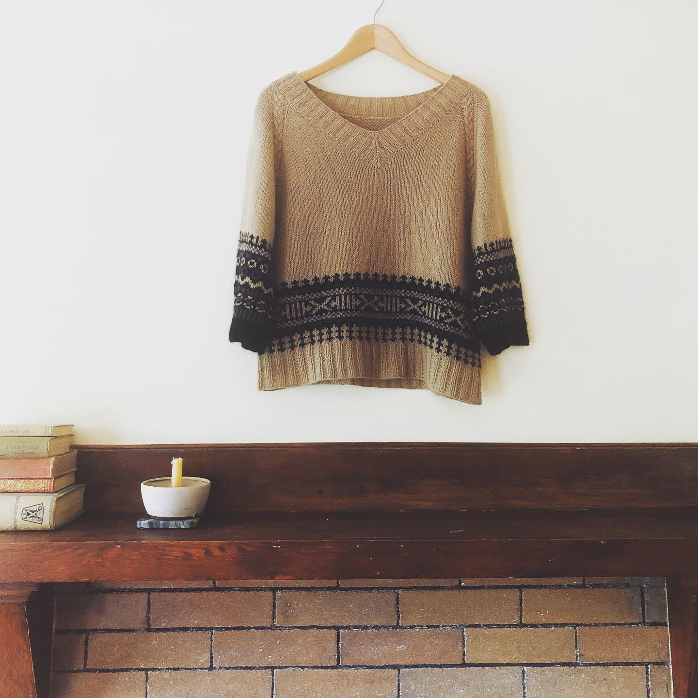 A colorwork pullover on a hanger hanging from a picture rail above a fireplace