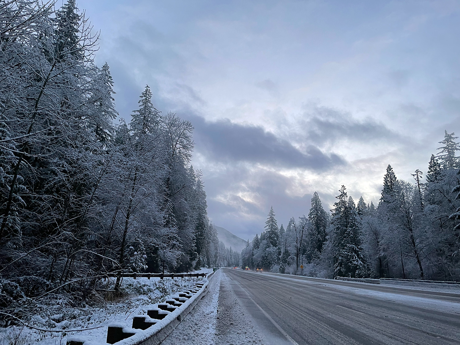 A photograph, facing east, of a mountain highway in the morning, a straggling line of cars heading toward the slopes